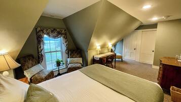 A bedroom with a large bed, a desk, and a chair. There is a window with curtains and a door in the background.