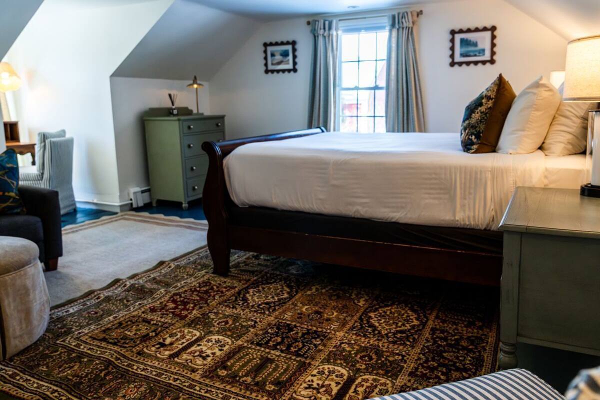 A bedroom with a large bed, a green dresser, a nightstand, and a window with curtains.