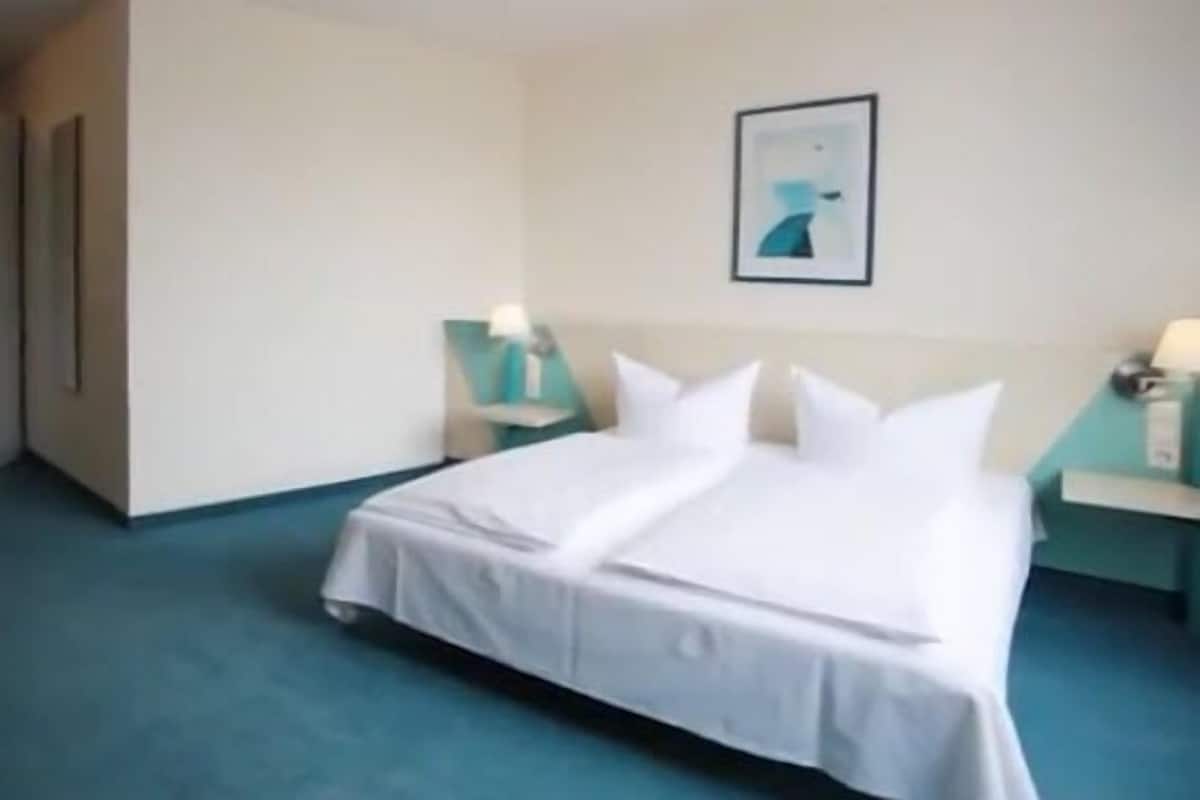 A hotel room with a large bed, two bedside tables with lamps, a chair, and a painting on the wall.