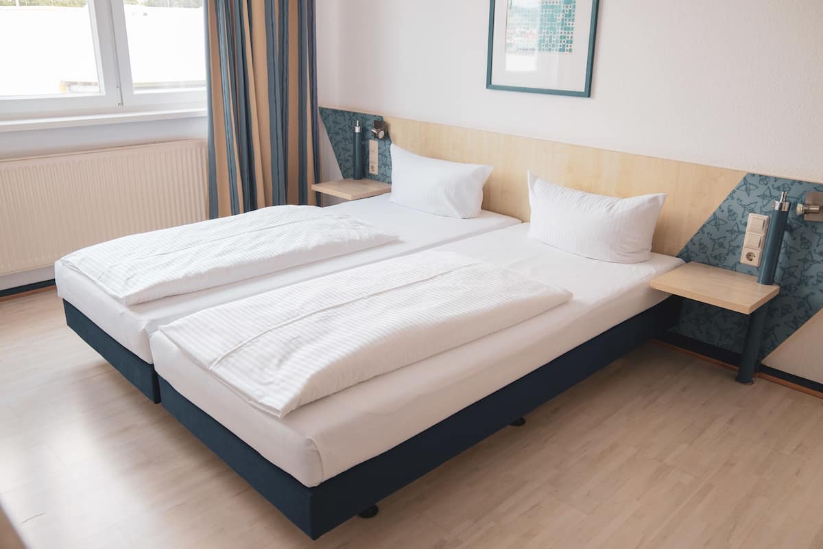 A double bed with white linens, a wooden headboard, and a bedside table with a lamp.