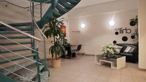 A modern interior with a spiral staircase, a seating area with a coffee table, and a wall with a logo. - Hotel Le Village (Winnenden)