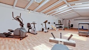 A spacious gym with various exercise equipment, high ceilings, and wooden flooring. - Hotel Le Village (Winnenden)