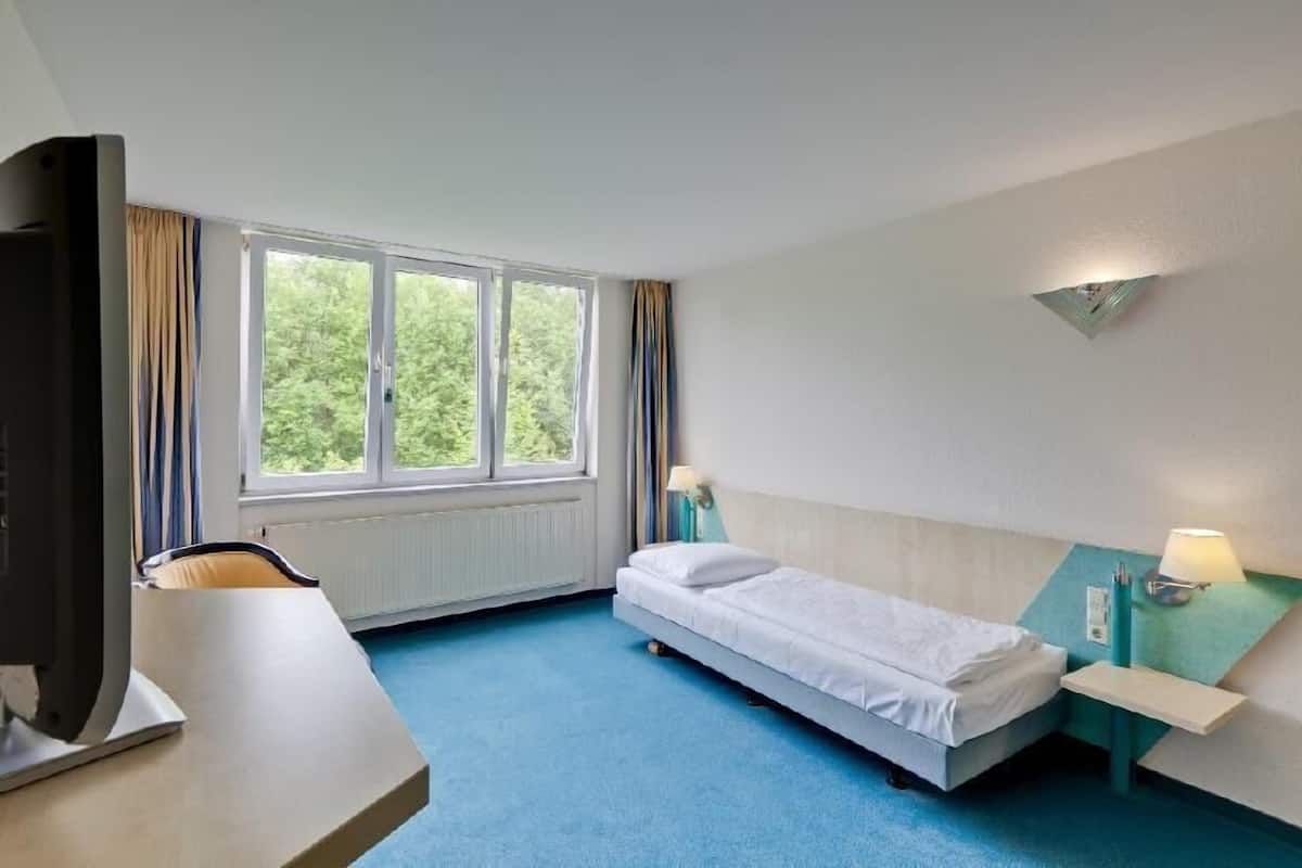 A hotel room with a bed, a desk, a chair, a TV, and a window with curtains.