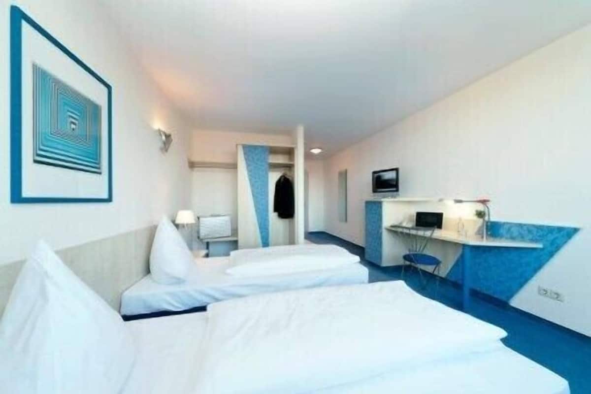 A hotel room with two beds, a desk with a computer, a TV, and a blue accent wall.