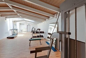 A spacious gym with wooden floors, exercise equipment, and a skylight. - Hotel Le Village (Winnenden)