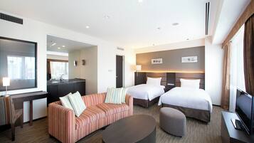 A hotel room with a sofa, two beds, a desk, a TV, and a bathroom.