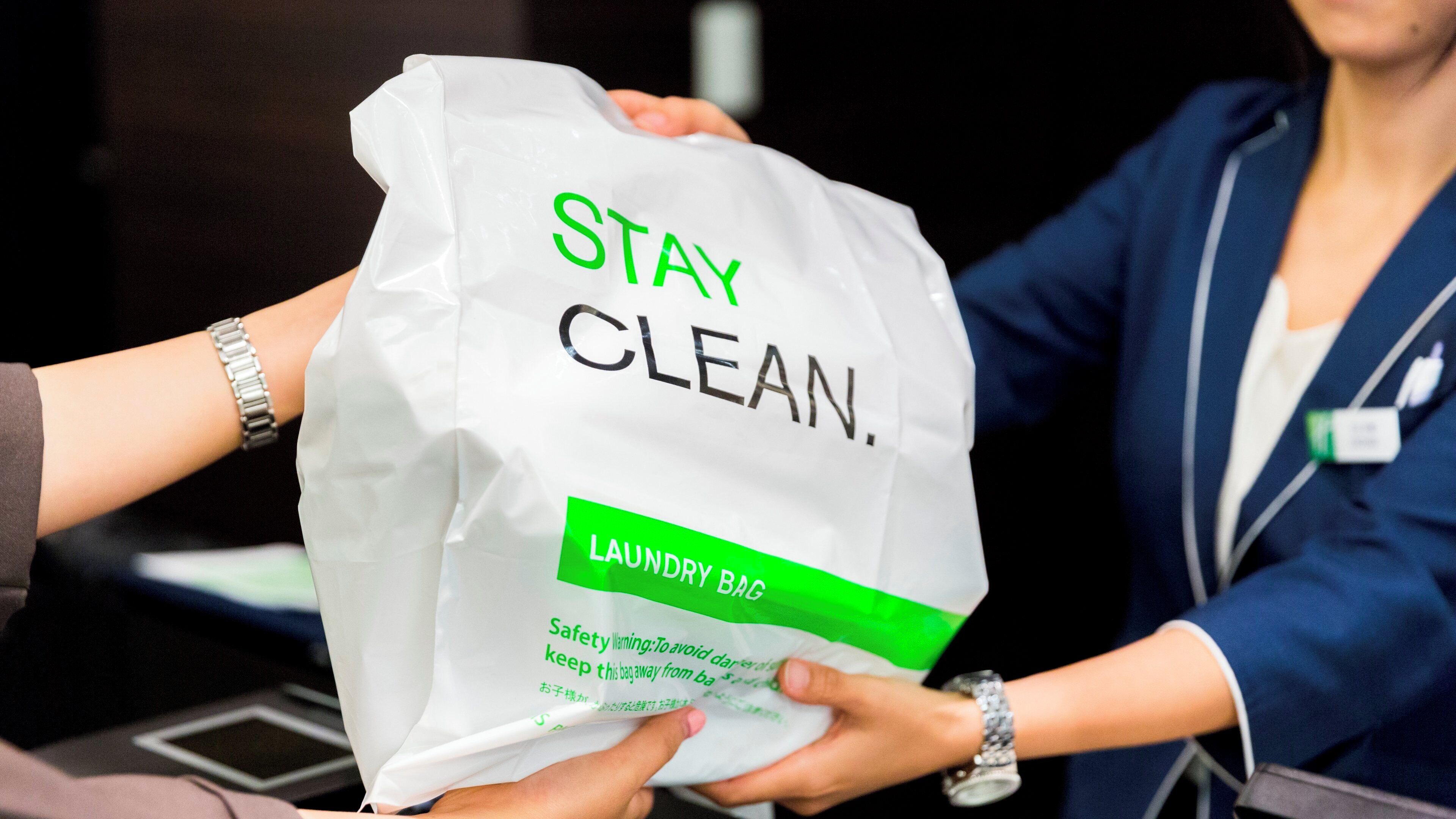 A person holding a white bag with 'STAY CLEAN' and 'LAUNDRY BAG' text.