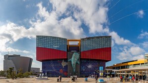 Een modern gebouw met een grote glazen gevel en een opvallende sculptuur van een dolfijn in het midden.