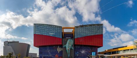 A modern building with a large glass facade and a distinctive dolphin sculpture at the center.
