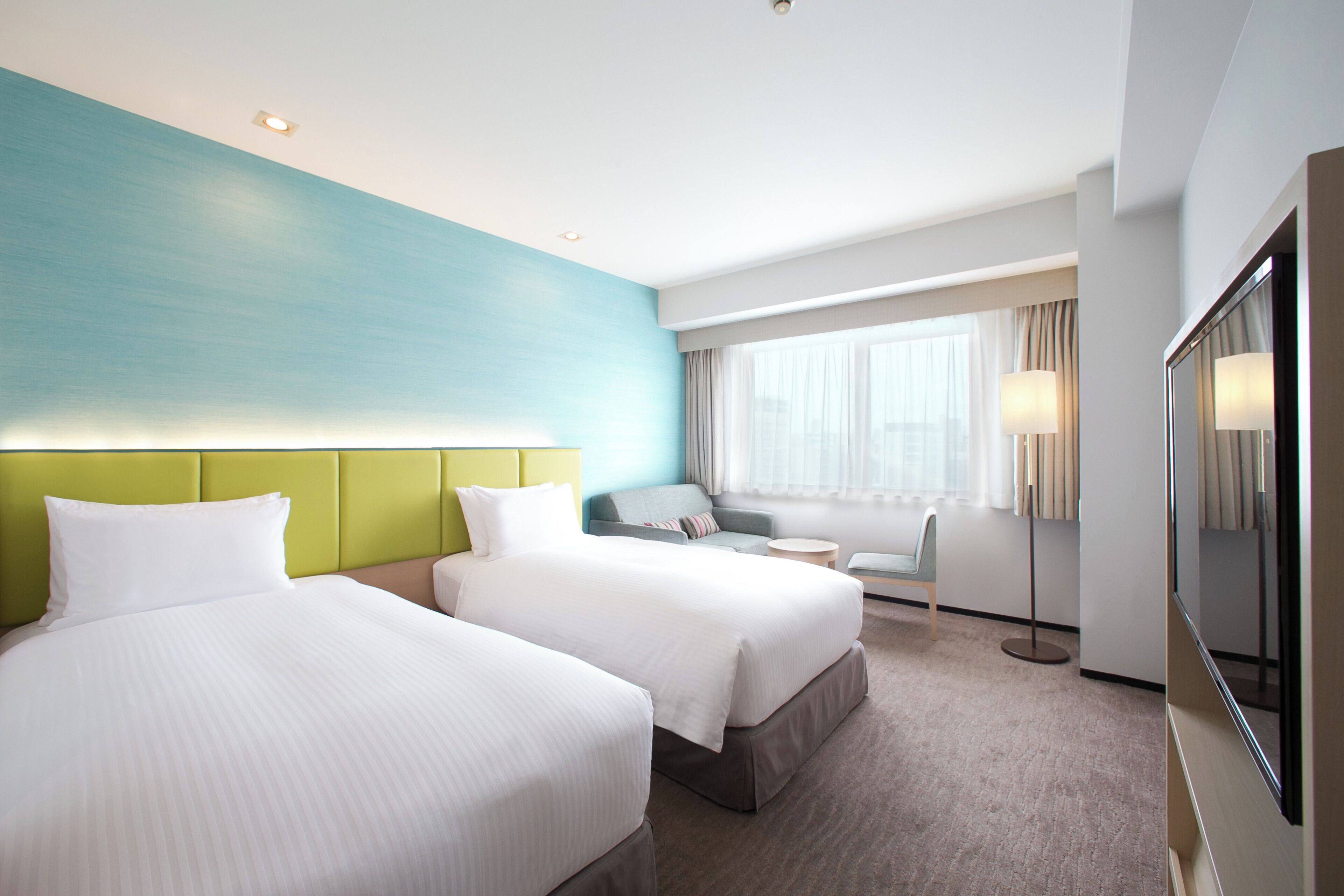Ein Hotelzimmer mit zwei Betten, einem Schlafsofa, einem kleinen Tisch und einem großen Spiegel.