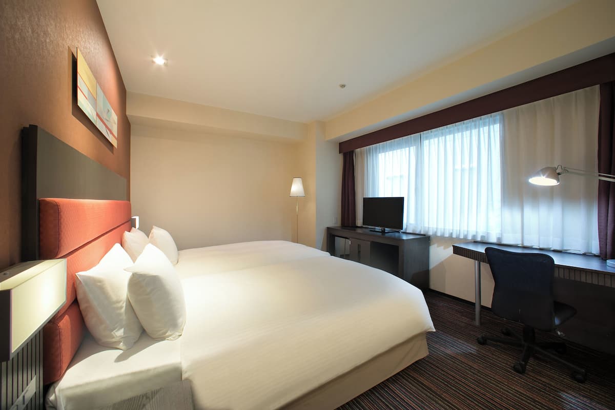 Camera d'albergo con un letto grande, una scrivania, una sedia, una televisione e una finestra con tende.