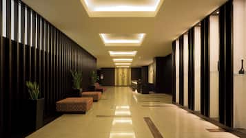 Vestíbulo de hotel con un largo pasillo, zonas de estar, mostrador de recepción e iluminación moderna.