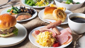 Uma mesa de café da manhã com vários pratos, incluindo ovos, bacon, um hambúrguer e um croissant.