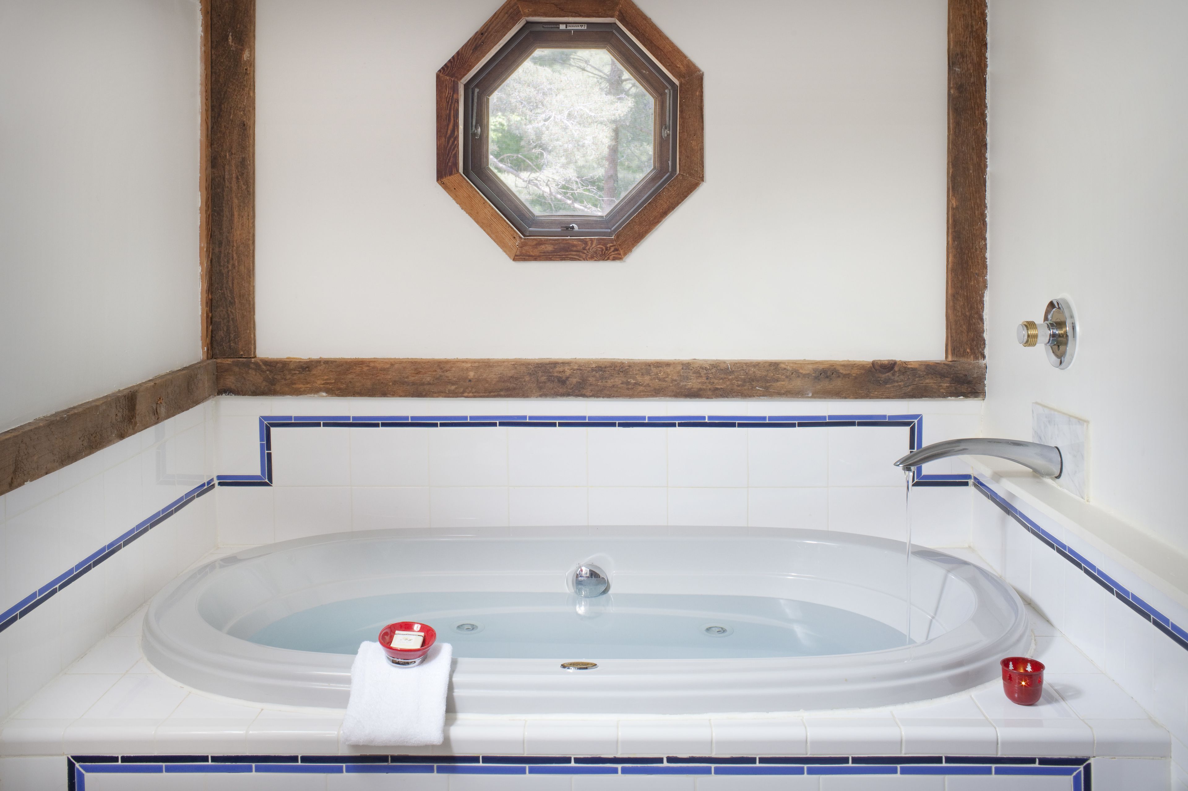 A large oval bathtub with a window above it, a towel, and a red cup on the side.