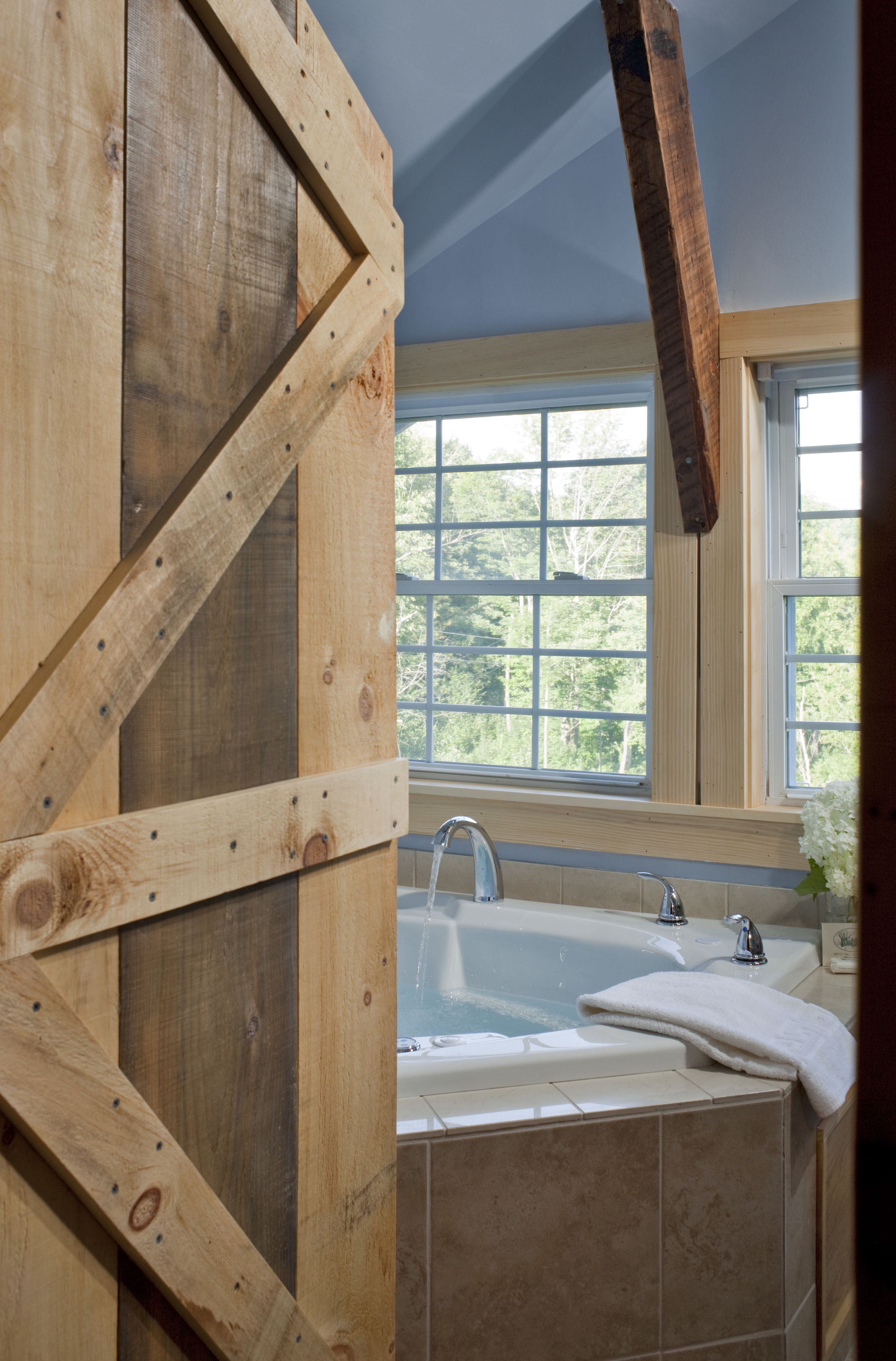 Ein Badezimmer mit Holzrahmen, einer Badewanne, einem Fenster mit Blick auf Bäume und einem Handtuch auf der Wanne.
