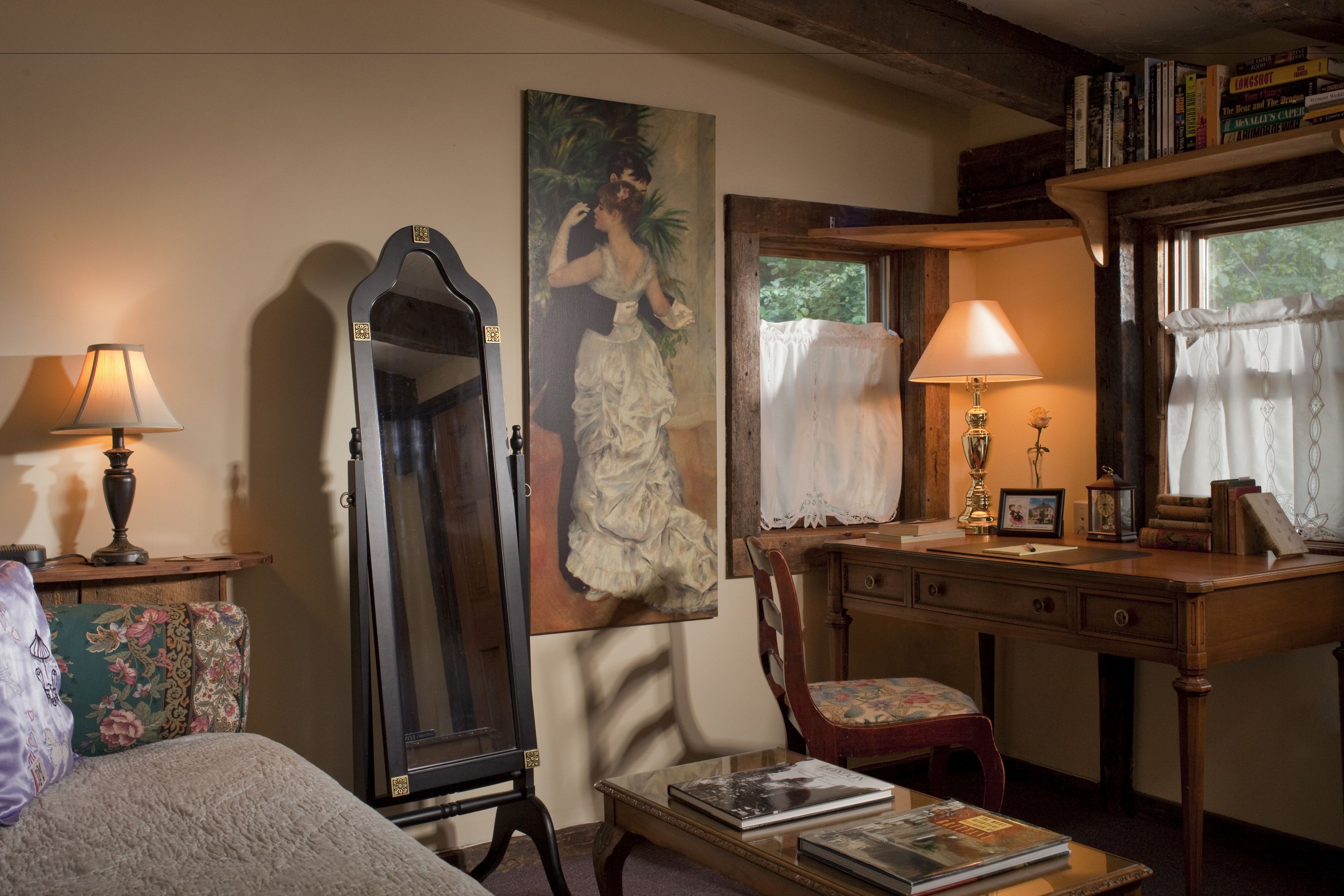 A room with a wooden desk, a chair, a bed, a mirror, and a painting on the wall.