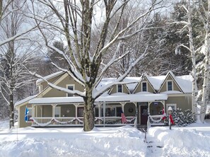 A two-story house with a porch, surrounded by snow-covered trees. - West Hill House B&B (Warren)
