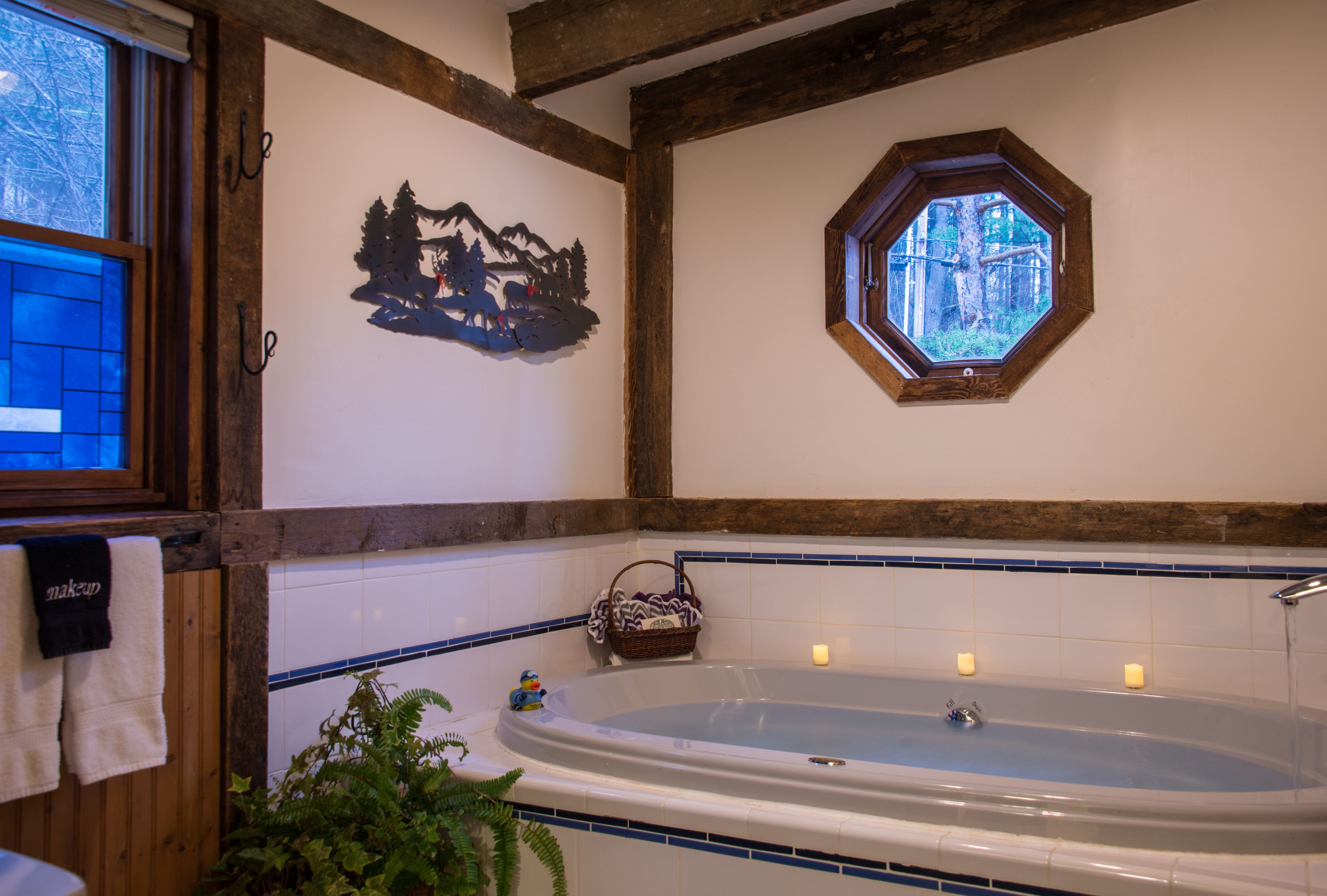 Un baño con una bañera grande, una ventana con vistas a árboles y un adorno en la pared.