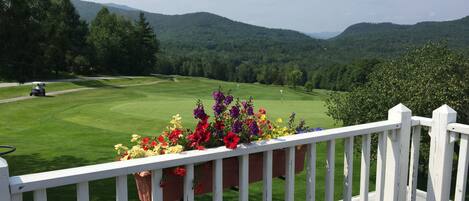A view of a golf course with a white railing and a planter with flowers.