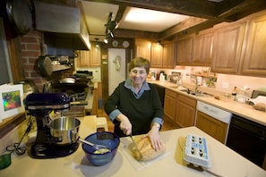 A kitchen with wooden cabinets, a mixer, a cutting board, and a person preparing food. - West Hill House B&B (Warren)