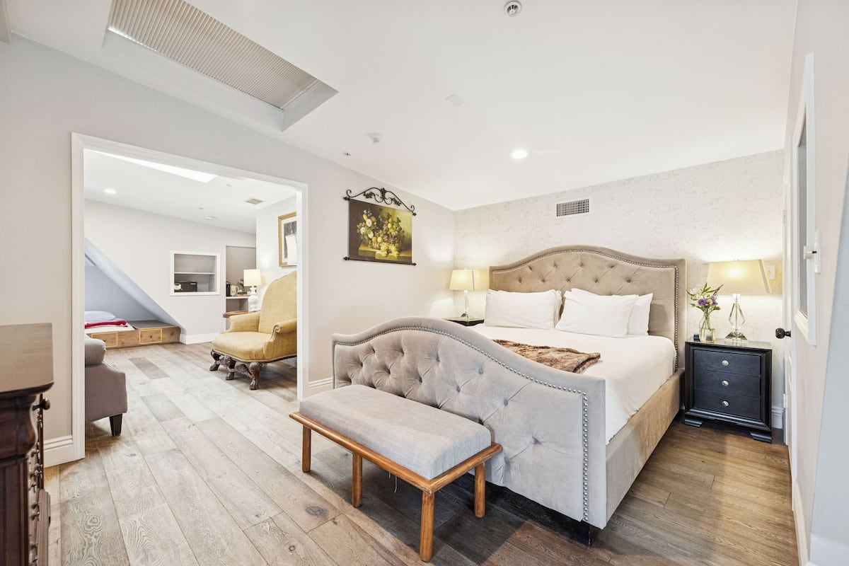 A bedroom with a large bed, bedside tables, a bench, and a staircase leading to another room.