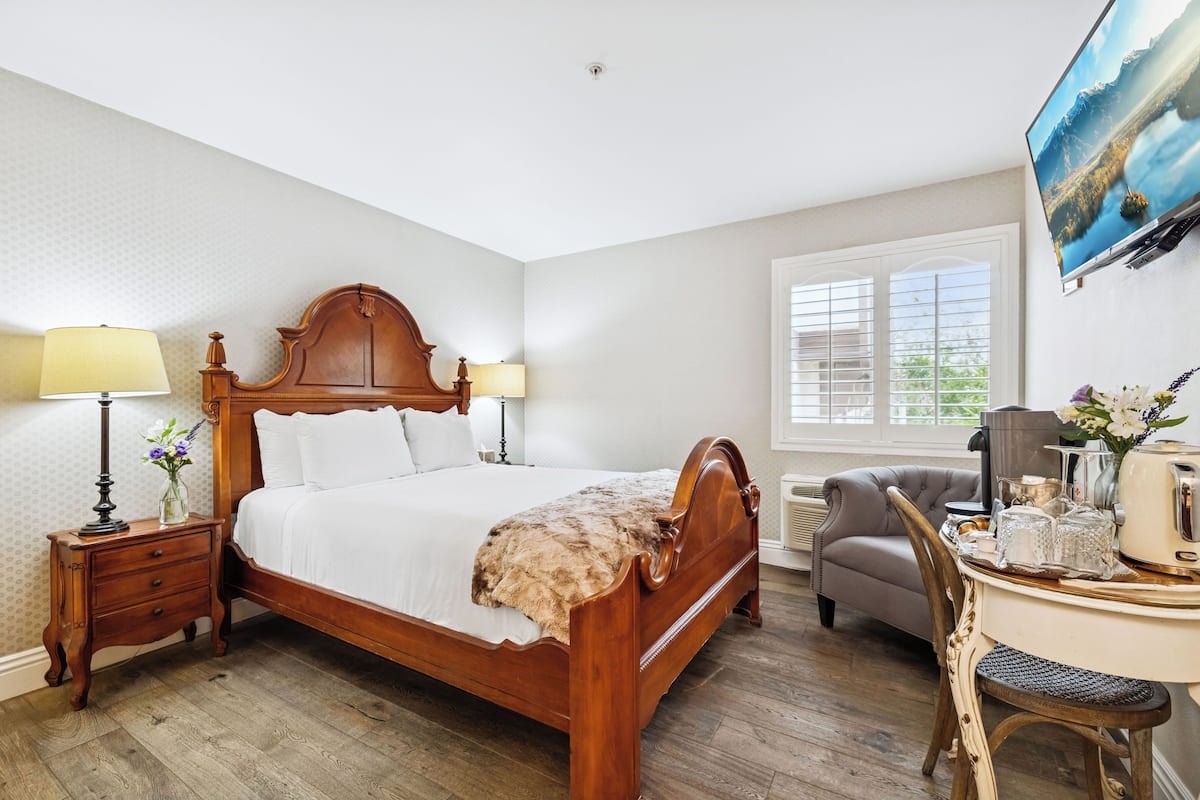 A neatly arranged bedroom with a wooden bed, bedside lamps, a desk with a chair, and a television on the wall.