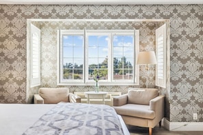 A bedroom with a large bed, two armchairs, a small table with a vase, and a window with shutters. - Mirabelle Inn (Solvang)