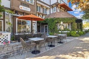 An outdoor cafe area with tables and chairs, a sign for Mirabelle Inn, and a building with ivy and stone walls. - Mirabelle Inn (Solvang)
