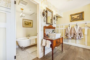 A bathroom with a freestanding bathtub, a vanity with a mirror, and a towel rack with robes. - Mirabelle Inn (Solvang)