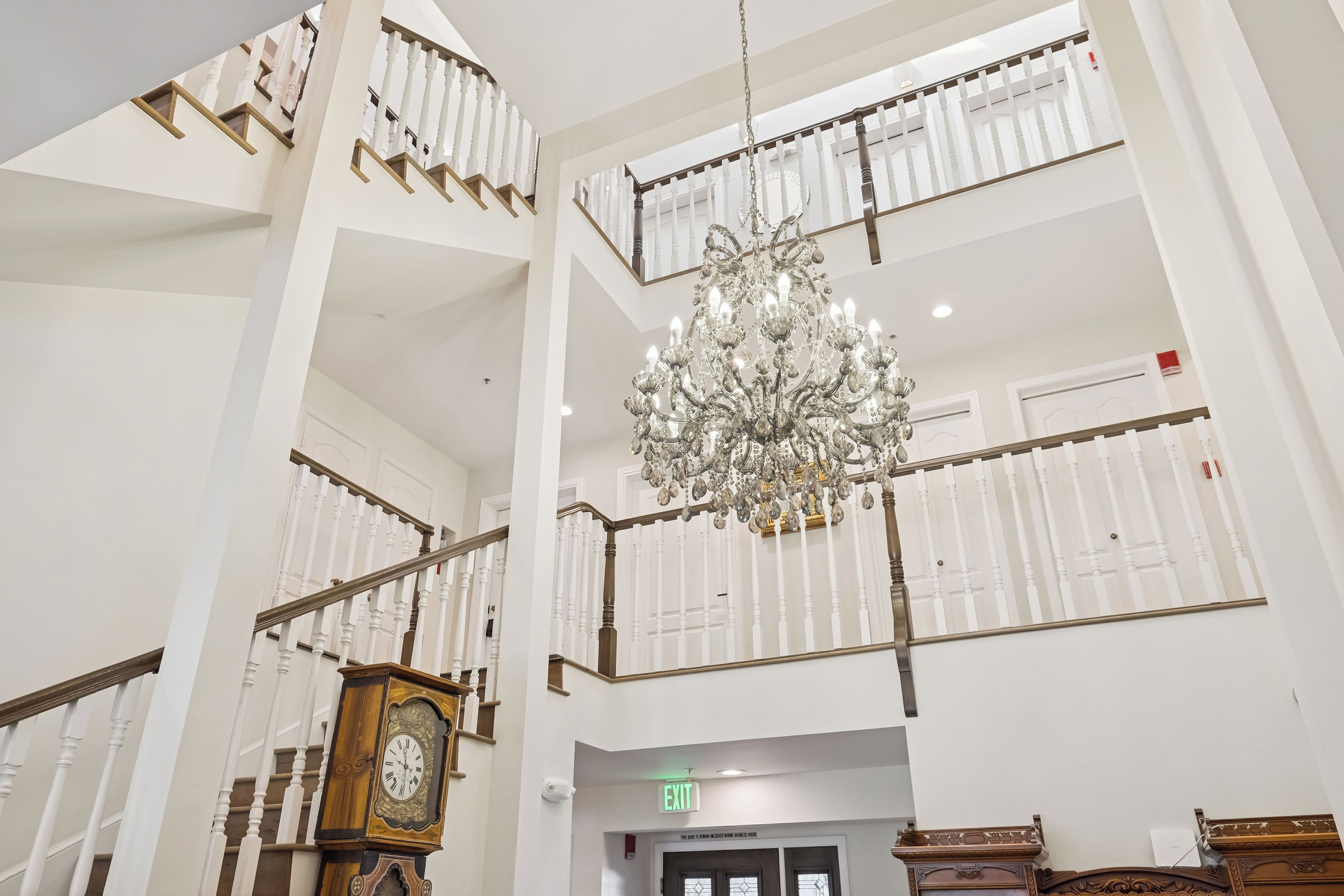 A multi-level hotel lobby with a grand chandelier, a wooden clock, and a staircase with white railings.