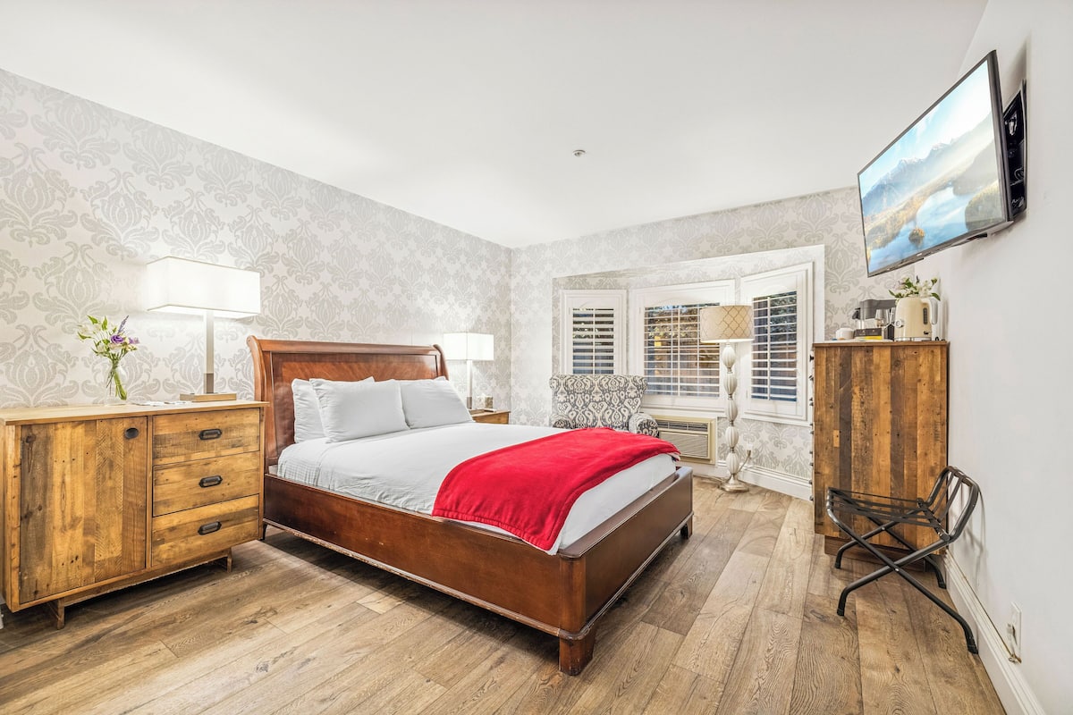 A bedroom with a wooden bed, a dresser, a chair, and a TV on the wall.