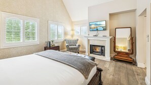 A bedroom with a large bed, a fireplace, a television, and a mirror. - Mirabelle Inn (Solvang)
