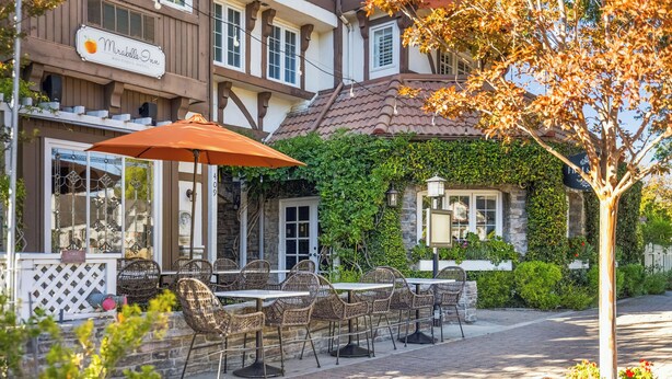 A restaurant with outdoor seating, a sign reading "Mirabelle Inn," and a tree with autumn leaves. - Mirabelle Inn (Solvang)