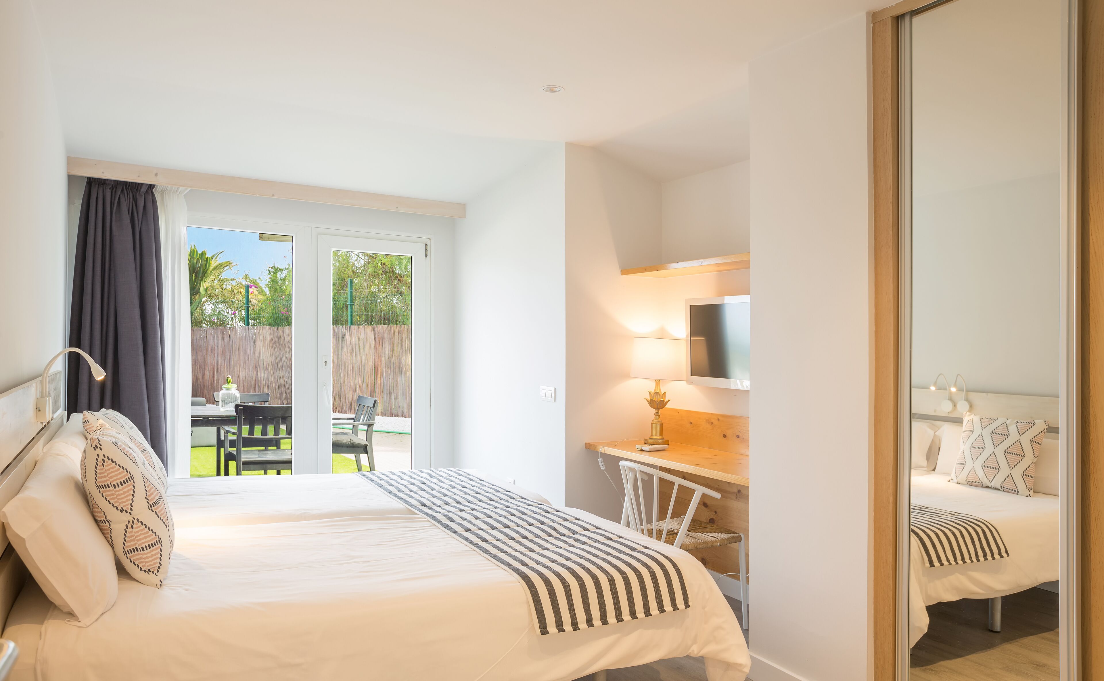 Une chambre à coucher comprenant un lit, un bureau, une chaise, un téléviseur et une porte-fenêtre coulissante donnant sur un patio.