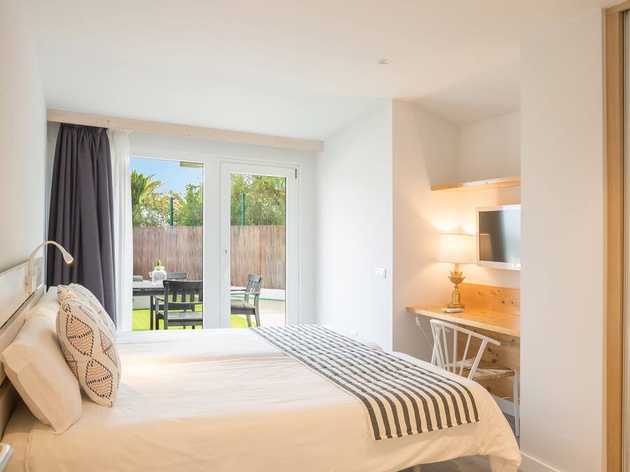 Une chambre à coucher comprenant un lit, un bureau, une chaise, un téléviseur et une porte-fenêtre coulissante donnant sur un patio.