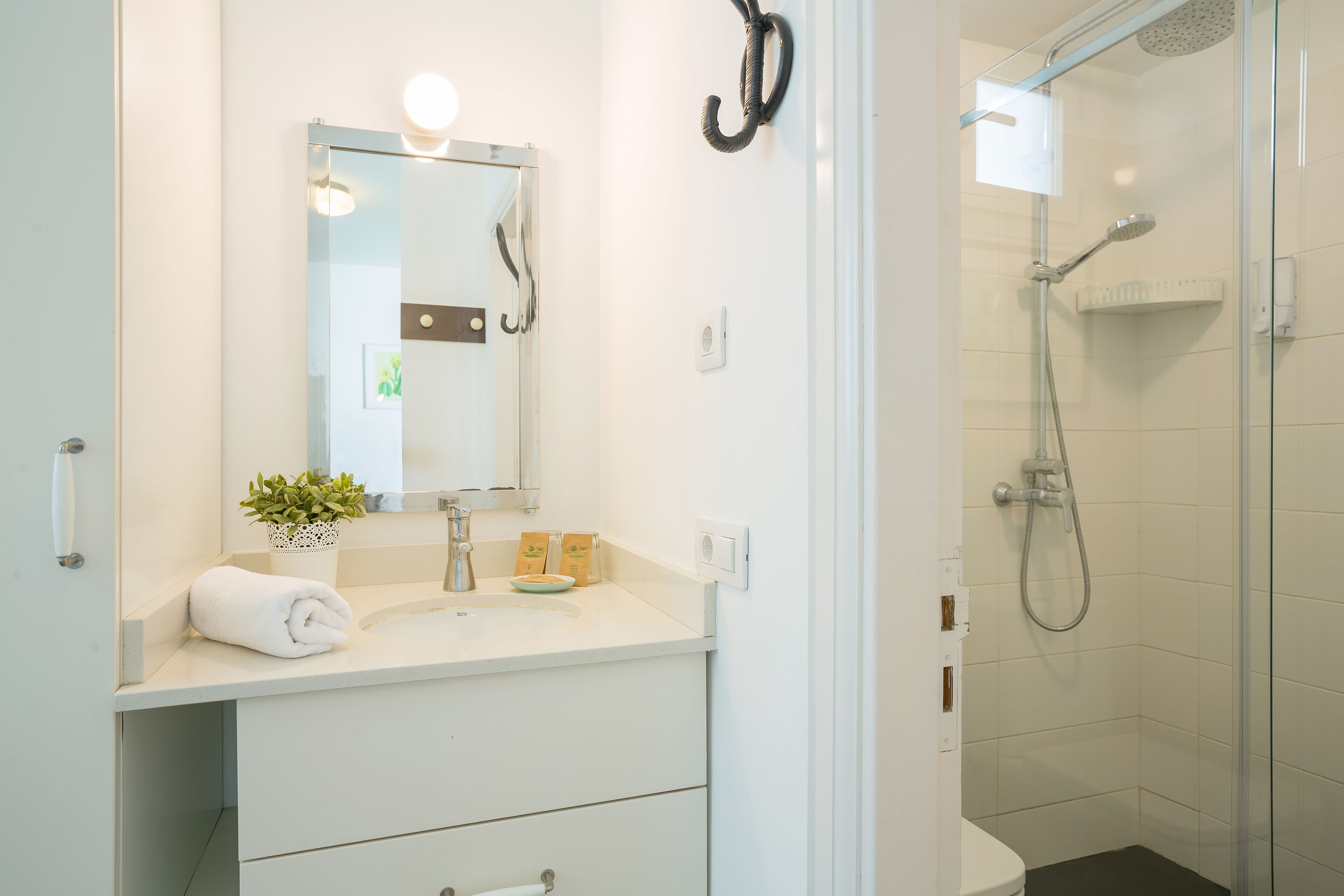 Een moderne badkamer met een witte wastafel, een spiegel, een handdoek, een klein plantje en een douchecabine met glazen wanden.