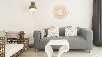 A modern living room with a grey sofa, patterned cushions, a wicker chair, a floor lamp, and a white coffee table.