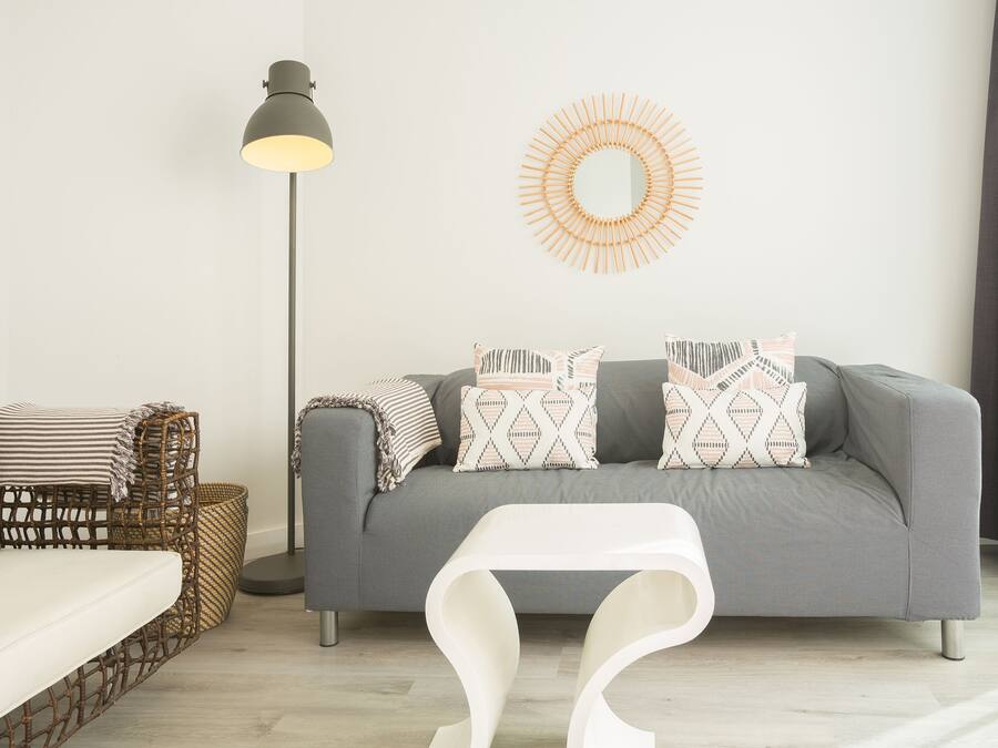 A modern living room with a grey sofa, patterned cushions, a wicker chair, a floor lamp, and a white coffee table.
