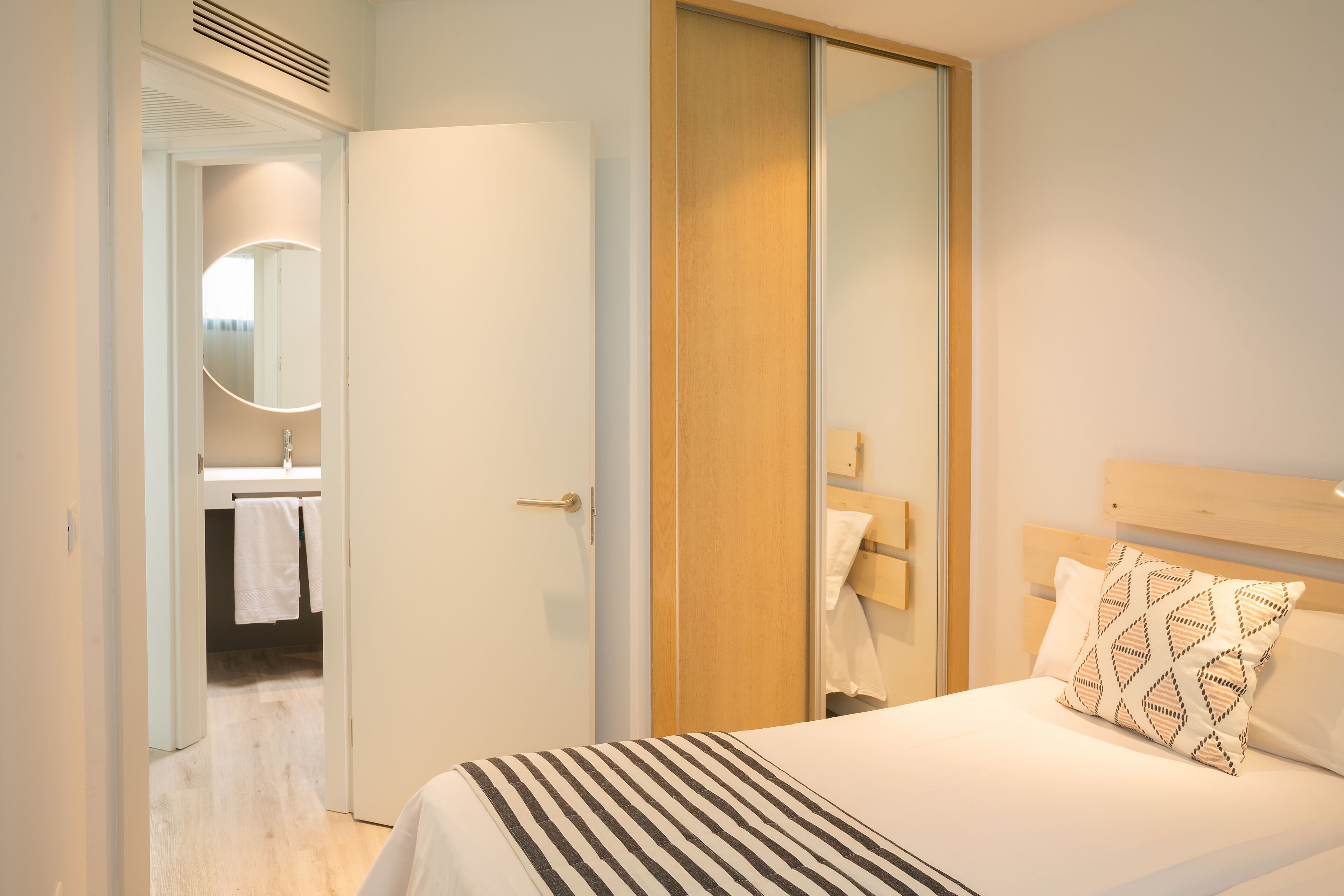 Une chambre d’hôtel comprenant un lit, une armoire en bois, une salle de bain avec un miroir et un lavabo, ainsi qu’un porte-serviettes.