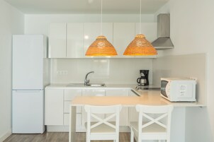 A modern kitchen with white cabinets, a double sink, a refrigerator, a microwave, and two pendant lights.