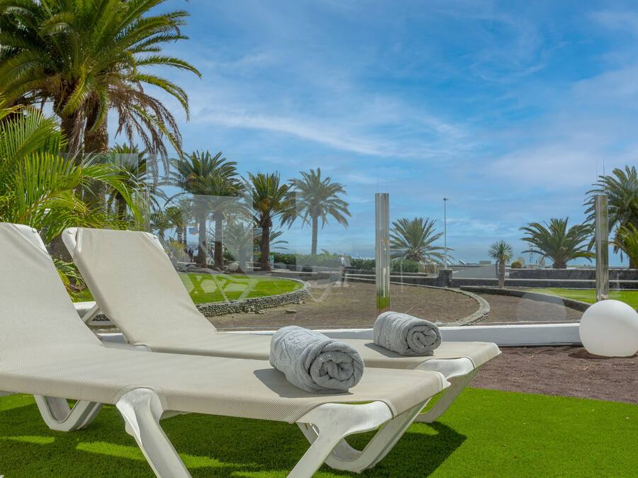 Zona de piscina con dos sillas de descanso blancas, cada una con una toalla enrollada.