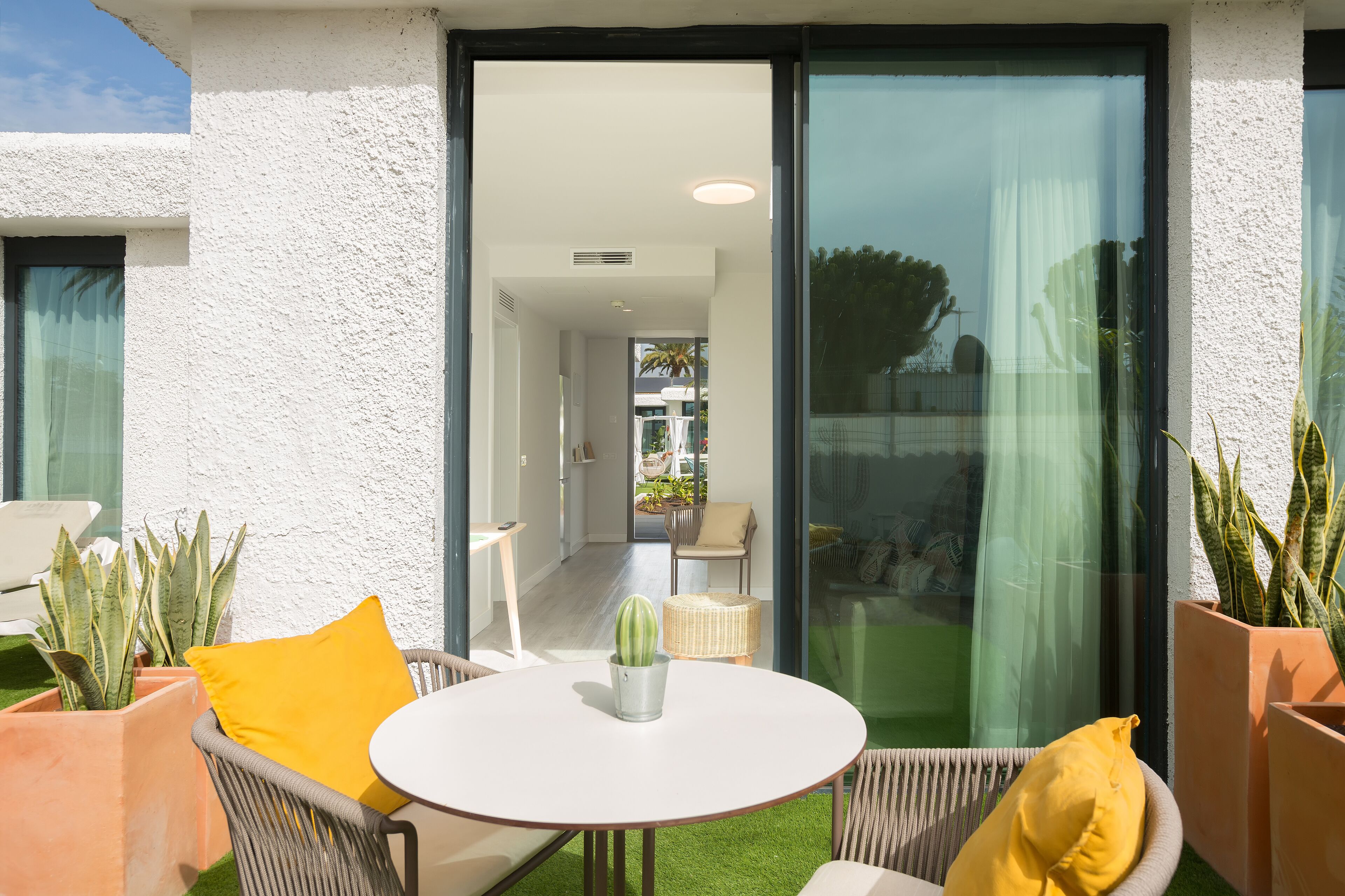 Een modern buitenterras met een ronde tafel, rieten stoelen en potplanten.