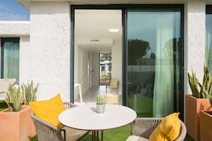Een modern buitenterras met een ronde tafel, rieten stoelen en potplanten.