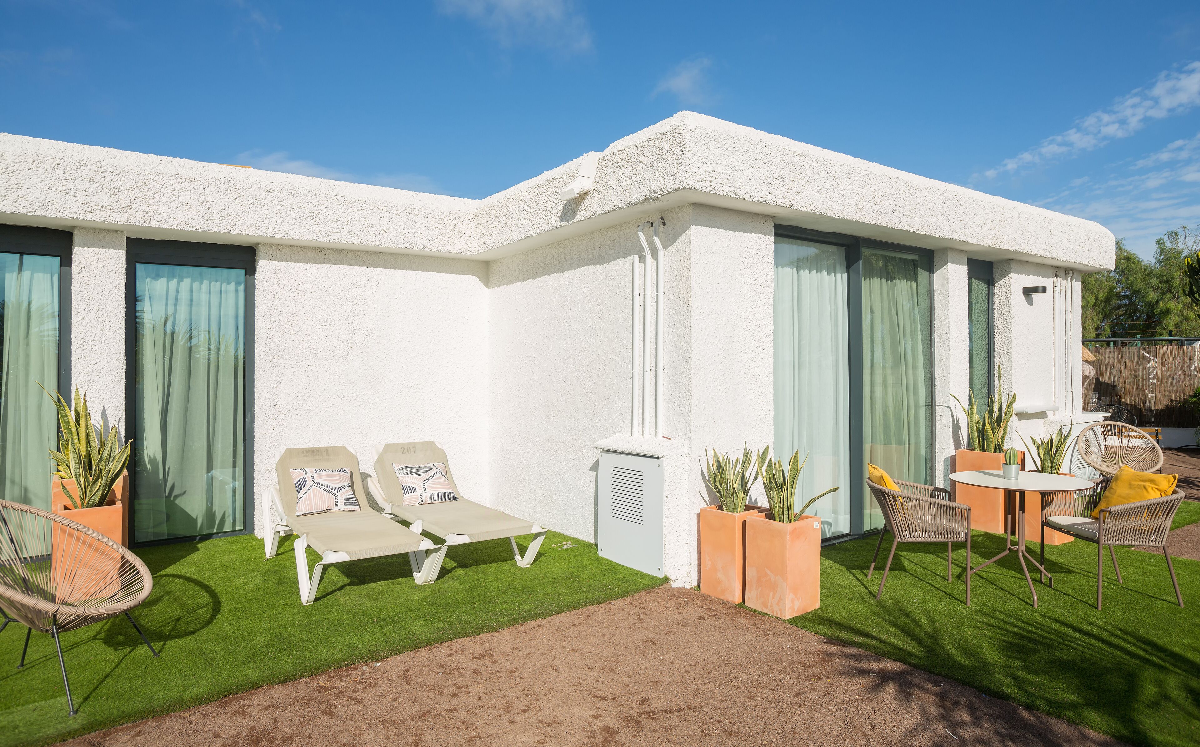 Un edificio blanco con dos sillones y una mesa en un área con césped.