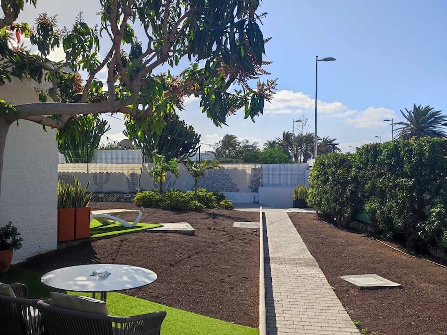 Un patio con sendero de ladrillo, césped verde y mobiliario exterior.