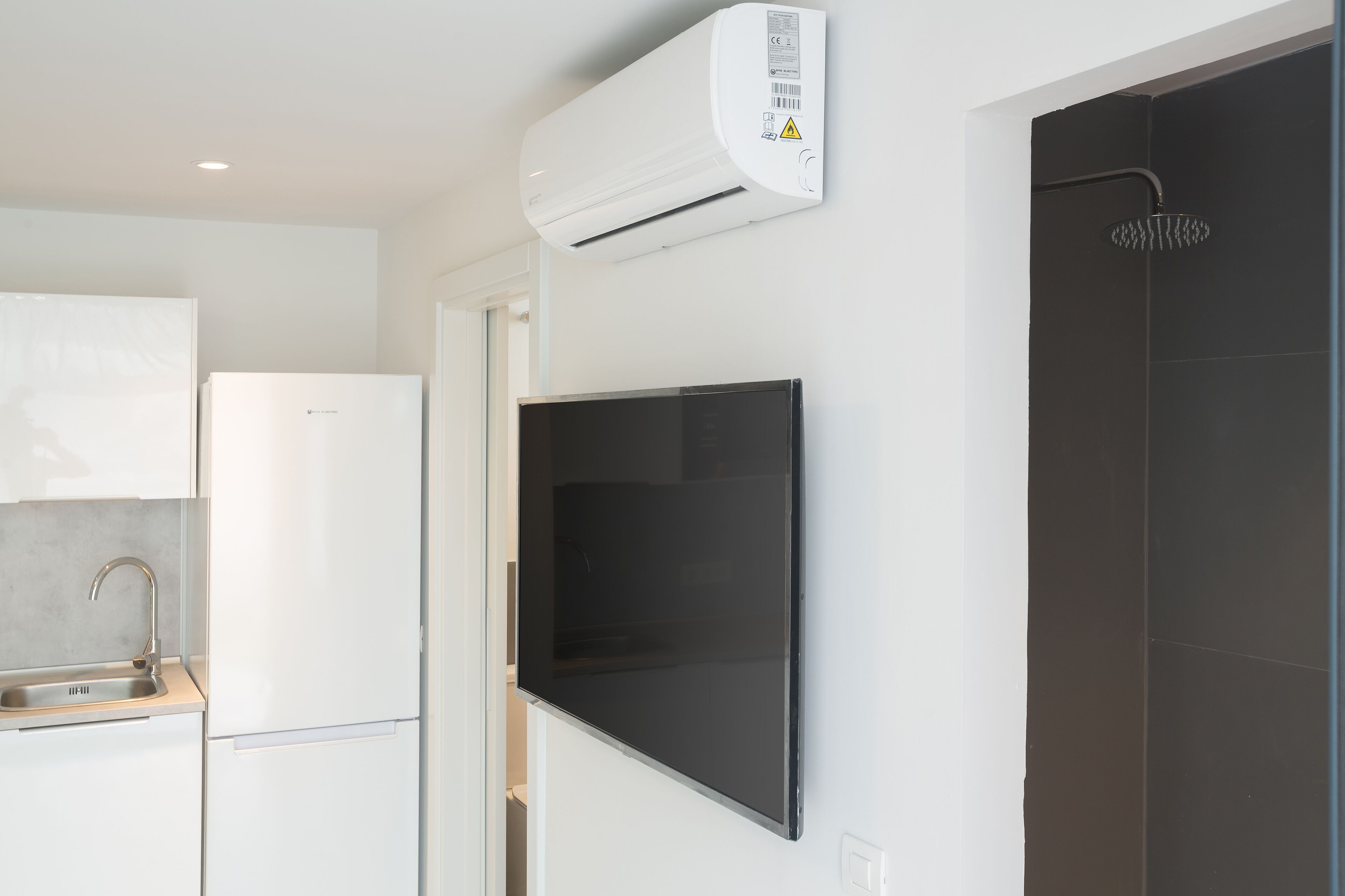 Eine moderne Küche mit einem eingebauten Kühlschrank, einem flachbildfernseher an der Wand und einer dunklen Duschkabine.