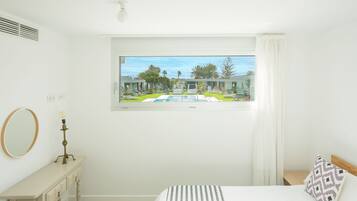 Quarto com uma janela grande, uma cama, mesa de cabeceira com abajur e um espelho.