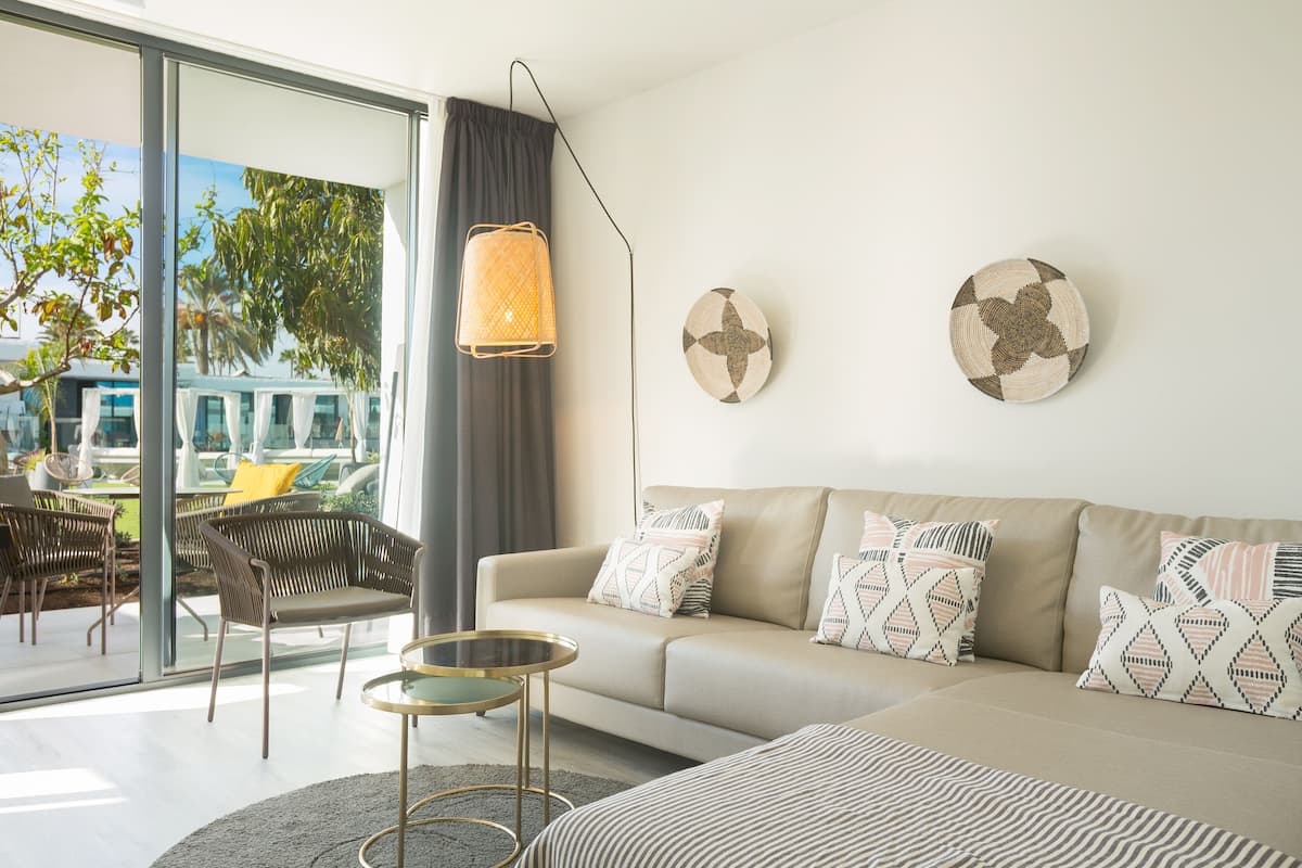 Una sala de estar moderna con un sofá, sillones, una mesa redonda y un amplio ventanal con vistas a muebles de exterior.