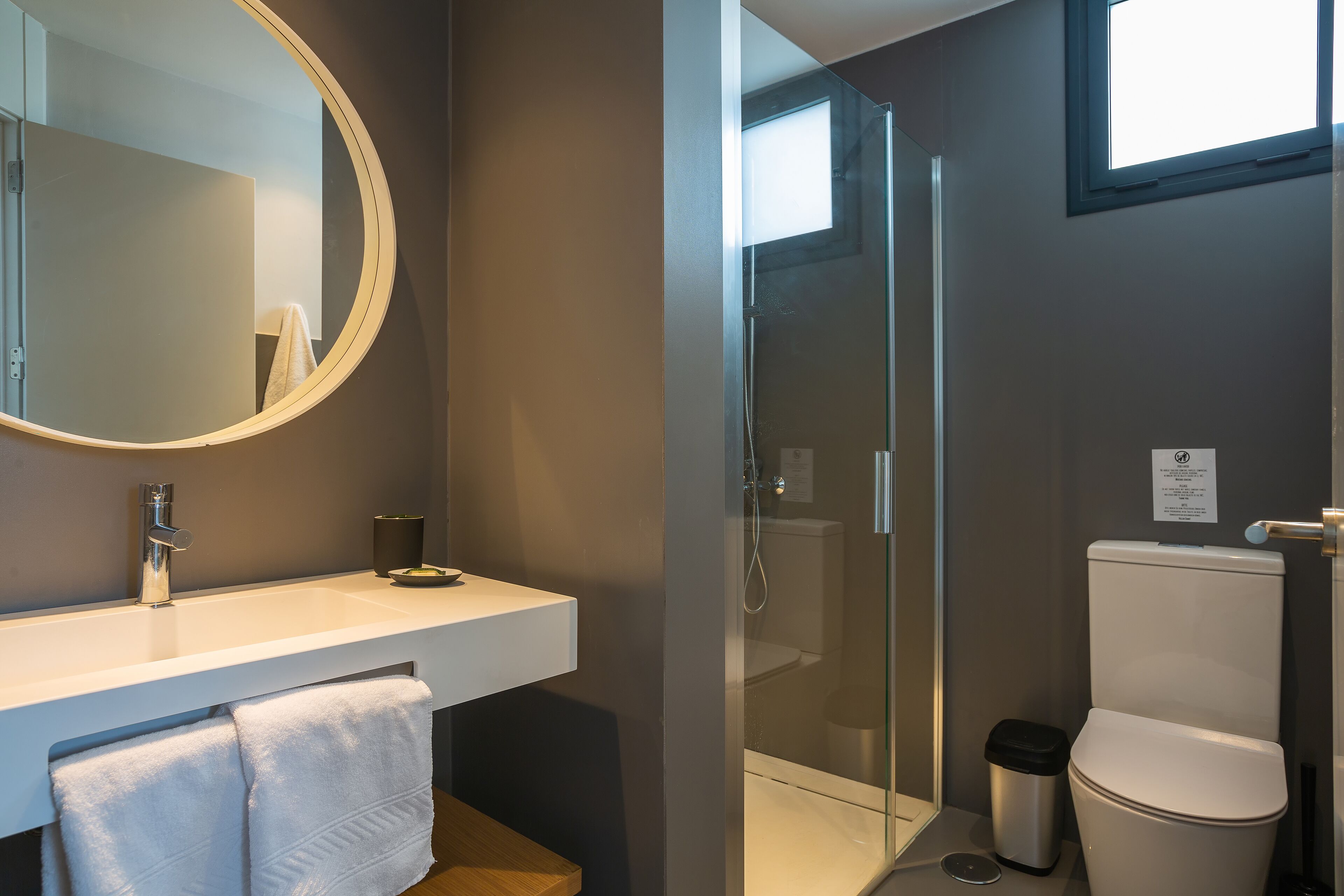 Un baño moderno con ducha de vidrio, un lavabo blanco con espejo y un inodoro.