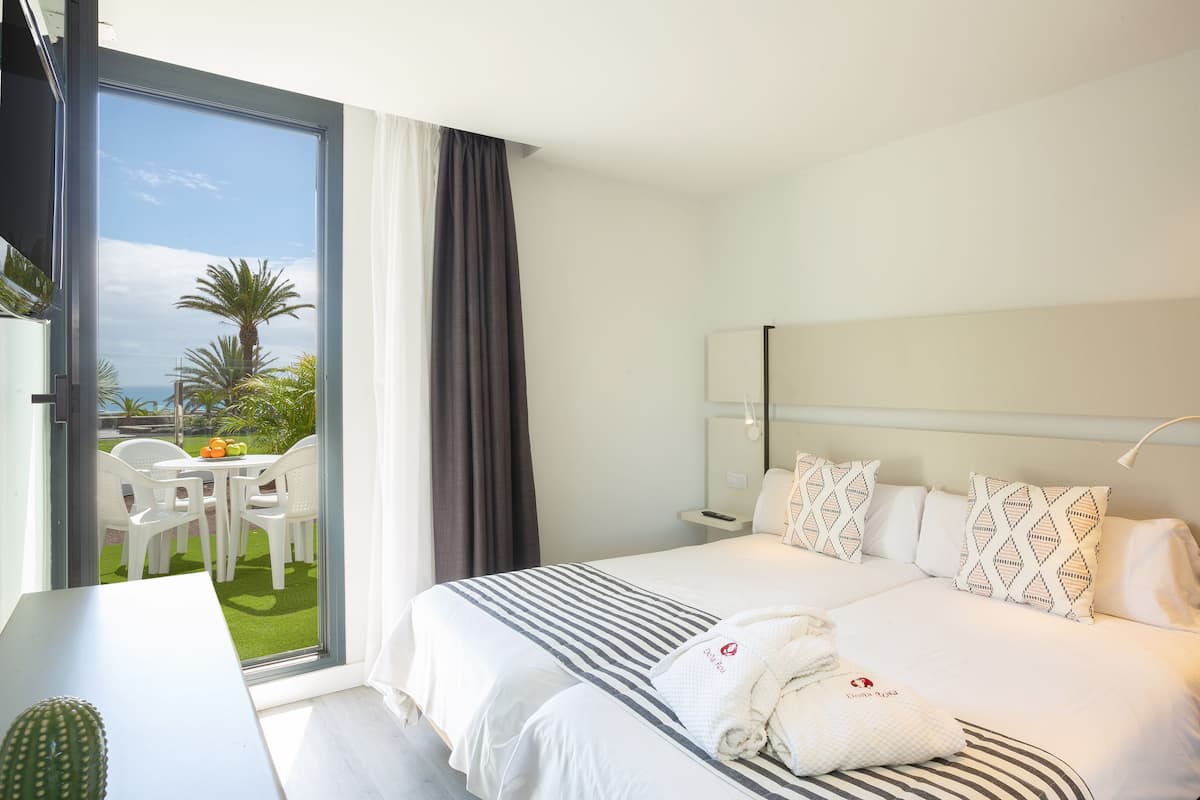 Habitación de hotel con cama, mesita de noche, lámpara, ventana con cortinas y vistas al exterior.
